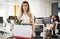 Fired female employee holding box of belongings in an office