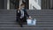 Fired male office worker in medical mask sitting on stairs in depression with box of stuff. Anxious concept. Workless