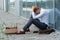 A fired office worker sits on the floor near a modern office building.