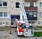 Firefighter begin to uprise into telescopic boom basket of fire truck, block of flats in background