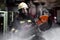 Firefighter portrait wearing full equipment, oxygen mask, and power hydraulic cutting tool, circular saw. smoke and fire trucks in