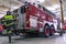 A firefighter in special clothes climbs onto the running board of a fire truck