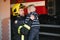 A firefighter take a little child boy to save him. Fire engine car on background. Fireman with kid in his arms