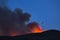 Firefighting plane soars from behind a hill in the darakness trailing a cloud of flame retardant