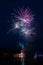 Fireworks launched from a river barge with lights reflected in the water.