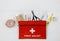 First aid kit in red bag on wooden table. Kit with patch, pills, scissors, masks, thermometer, elastic bandages. Top view,