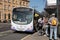 First branded bus in corporate livery at bus stop to pick up passengers in sunshine.  Public transport in urban environment