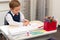 A first grader boy draws a postcard for the holiday of halloween with a red bright pencil on a white sheet of paper while sitting