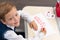 A first grader boy draws a postcard for the holiday of halloween with a red bright pencil on a white sheet of paper while sitting