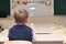 First grader boy at his desk in the classroom on the day of knowledge at school. There is an inscription on the blackboard - for t