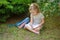 First grader sits having crossed legs under a tree and does homework.