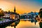 The first light of day kissing a Swiss riverside village, casting a golden hue on the quaint houses and the calm waters of the