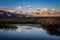 First morning light illuminates mountains trees in silhouette and reflection in water