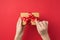 First person top view photo of female hands untying red ribbon bow on craft paper giftbox on  red background