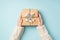 First person top view photo of female hands in white sweater holding craft paper giftbox decorated with snow twig and twine on