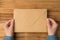First person top view photo of hands holding closed craft paper envelope on isolated wooden table background with copyspace