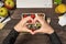 First person top view photo of hands making heart with fingers over two lunchboxes with salad berries nuts apples glass of juice