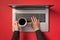 First person top view photo of hands typing on laptop keyboard and holding cup of drinking on isolated red background