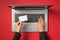 First person top view photo of hands typing on laptop keyboard and holding small rectangular white card on isolated red background