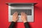 First person top view photo of hands typing on laptop keyboard on isolated red background