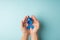 First person top view photo of man`s hands holding blue ribbon with small red heart in palms symbol of prostate cancer awareness