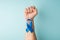 First person top view photo of raised male hand with clenched fist and blue ribbon on wrist symbol of prostate cancer awareness on