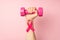 First person top view photo of raised woman`s hand holding pink dumbbell and pink ribbon on wrist symbol of breast cancer