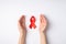 First person top view photo of red ribbon between palms symbol of aids awareness on  white background