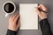 First person top view photo of woman`s hands holding pen open copybook cup of coffee on  grey background with blank space