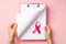 First person top view photo of woman`s hands holding pink clipboard and turning page pink ribbon symbol of breast cancer awarenes