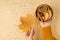 First person top view photo of woman`s hands in yellow pullover holding yellow maple leaf and wooden bowl with cookies dried lemo