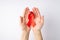 First person top view photo of young girl`s hands holding red silk ribbon in palms symbol of aids awareness on  white