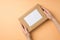 First person top view photo of young woman`s hands giving kraft paper giftbox with paper sheet on isolated beige background with