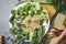 First person view on a dish with raw buckwheat sprouts, broccoli, sticks of asparagus beans, cucumber, avocado, spinach and seeds