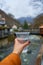 First-person view holding a glass of pure water from a mountain spring against the background of the city of Borjomi