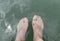 First person view of male feets into lake water with small fishes swimming around