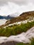 First snow on Alpine meadow, cascade on stream. Peaks of Alps mountains in background. Foamy water is running down over stones.