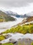 First snow in Alps touristic region. Fresh green meadow with rapids stream. Peaks of Alps mountains in background.