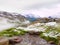 First snow in Alps touristic region. Fresh green meadow with rapids stream. Peaks of Alps mountains in background.