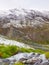 First snow in Alps touristic region. Fresh green meadow with rapids stream. Peaks of Alps mountains in background.