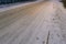 The first snow fell on the road and sidewalk. A footpath with tracks and a road for cars not cleared of snow. Winter morning