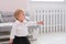 First steps of baby girl learning to walk in white sunny bedroom