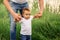 First steps: father supporting toddler son, making first steps in high grass outdoors. Parental support and confidence concept