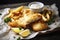 A fish and chips dish with crispy fries and a side of tangy tartar sauce is served on a newspaper tray. (Generative AI)