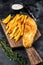 Fish and chips dish with french fries on wooden board. Black background. Top view