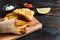 Fish and chips in a paper cone on wood chopping board dip and lemon - fried cod, french fries, lemon slices, tartar sauce, ketchup