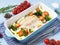 Fish cod baked in blue oven with vegetables - broccoli, tomatoes. Healthy diet food. Blue stone background, side view.