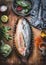 Fish dish cooking preparation. Two Trout fishes in baking form on wooden rustic kitchen table background with vegetables and condi