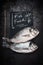 Fish food lettering on black chalkboard with two raw whole dorado fishes on dark vintage background, top view. Seafood