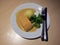 Fish meat topped with sauce and boiled broccoli, one scoop of mash potato with Knife and fork in the white dish.